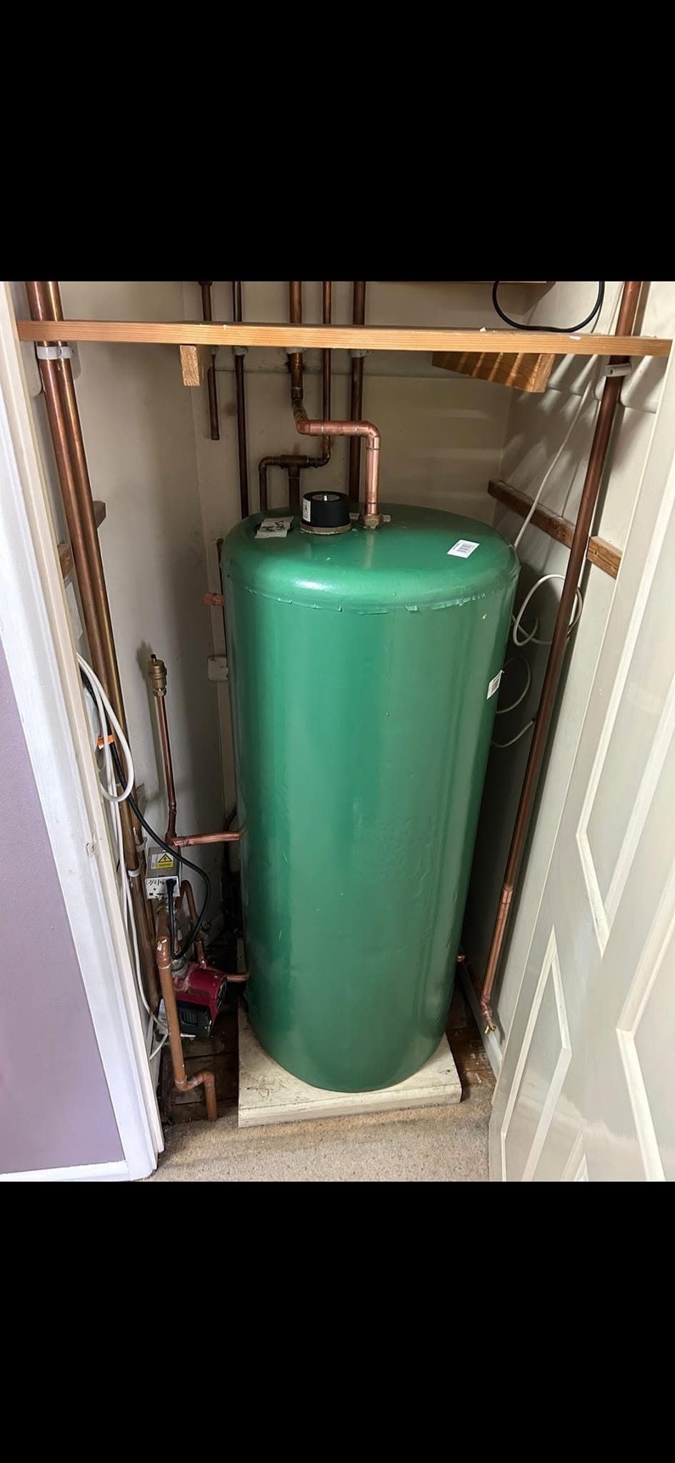 Green vented hot water cylinder with copper pipework in airing cupboard